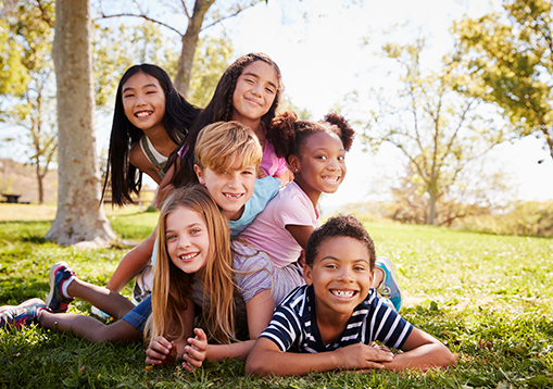 Multi-ethnic group of kids lying on each other in a park